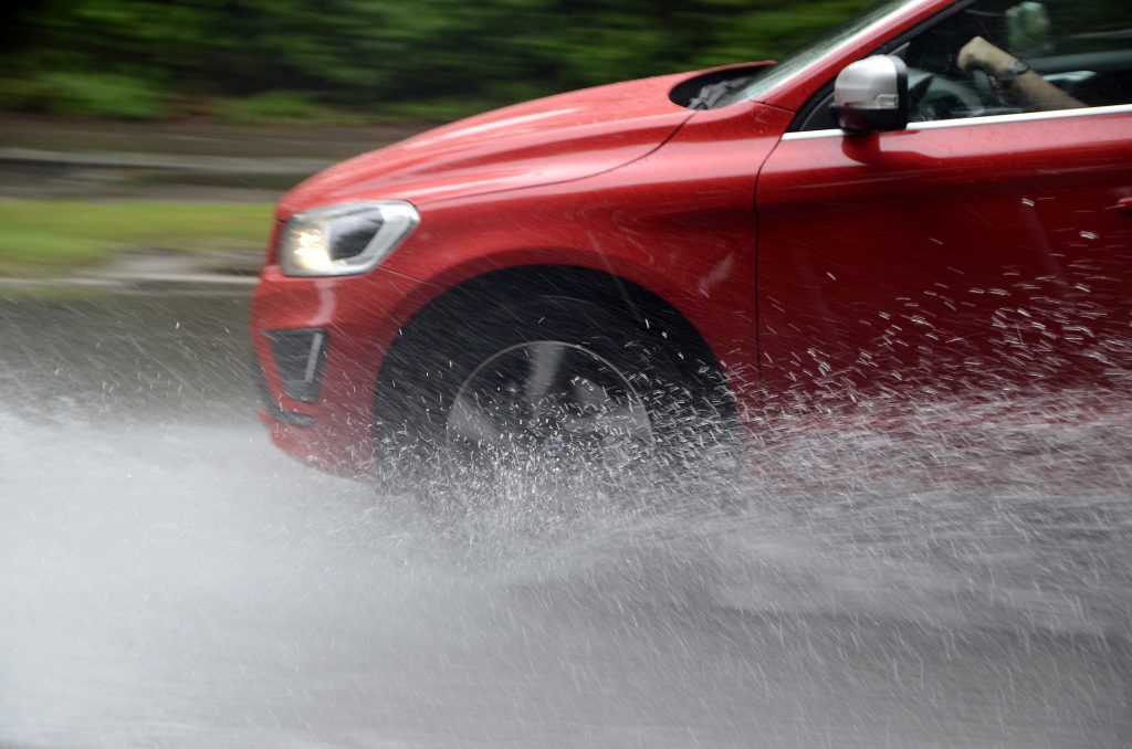 Červené auto na mokré vozovce s vodou stříkající od pneumatik v aquaplaningu.
