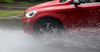 Červené auto na mokré vozovce s vodou stříkající od pneumatik v aquaplaningu.