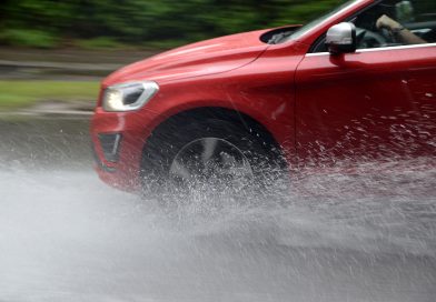 Červené auto na mokré vozovce s vodou stříkající od pneumatik v aquaplaningu.