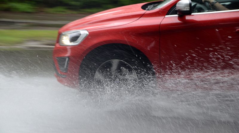 Červené auto na mokré vozovce s vodou stříkající od pneumatik v aquaplaningu.