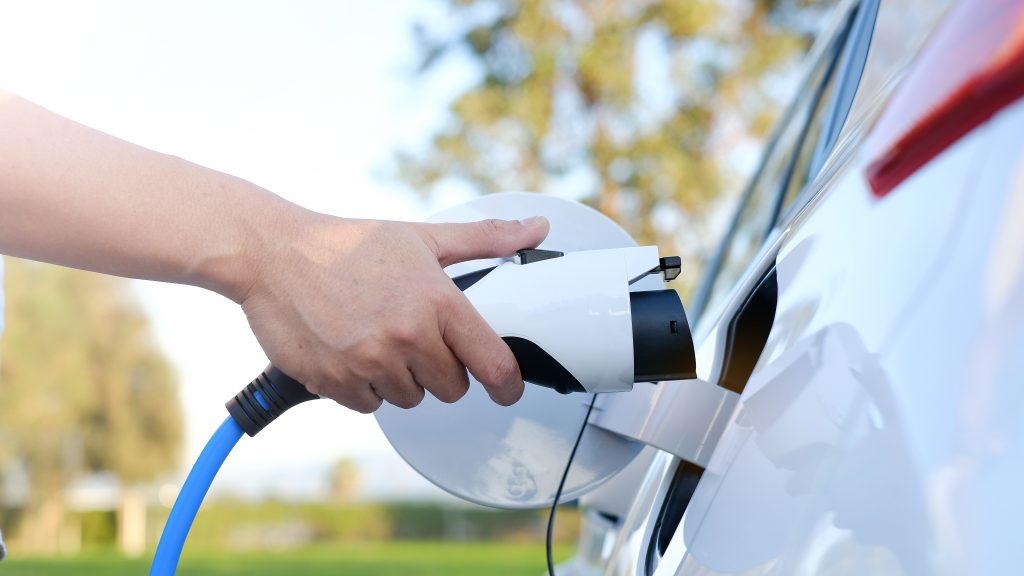 Muž držící nabíječku u bíleho plug-in hybridu.
