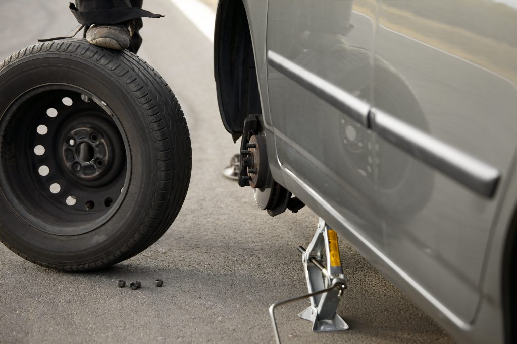 Muž mění pneumatiku na osobním automobilu.
