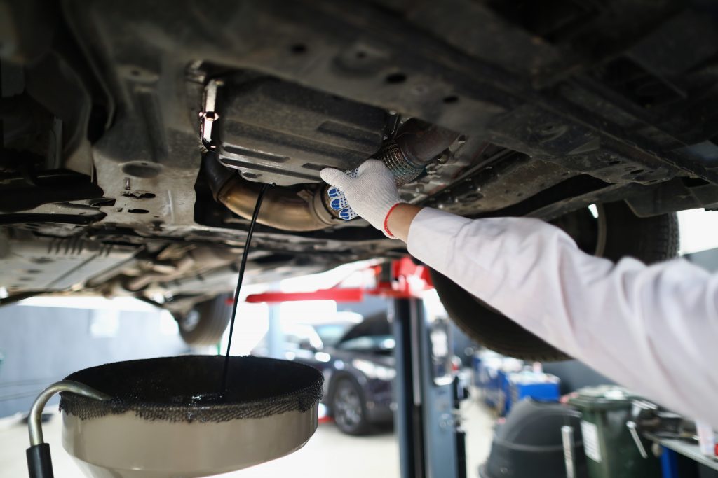 Automechanik měnící starý olej z osobního automobilu.