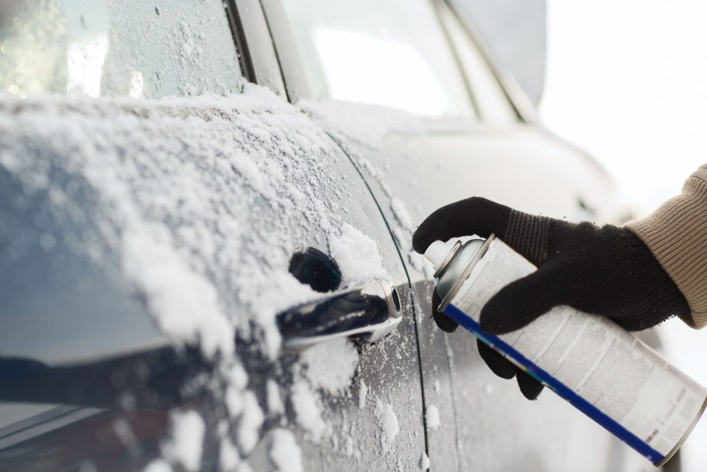 Stříkání dveří sprejem proti rzi na tmavém osobním automobilu.